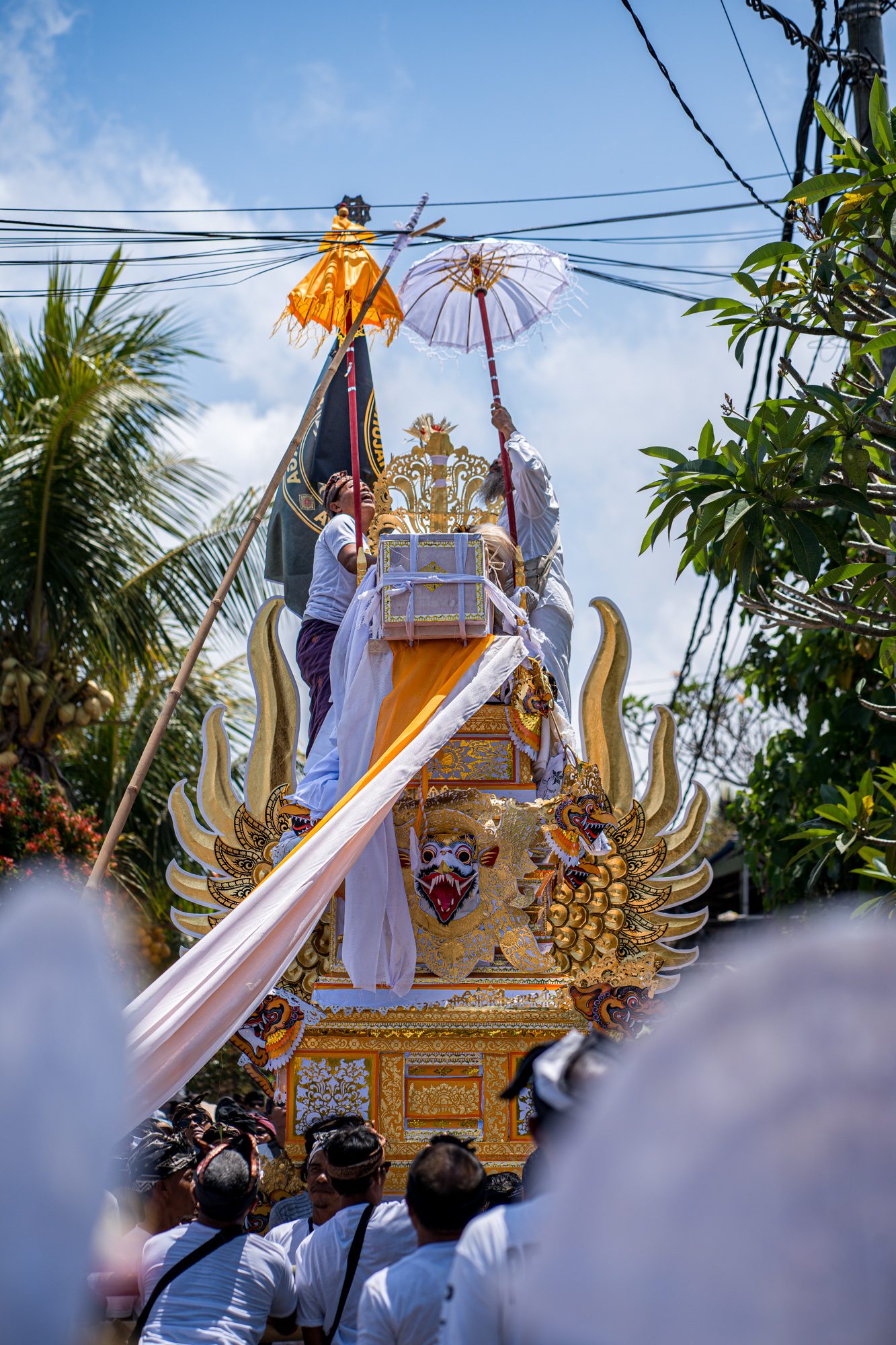 Officiants au sommet de la tour funéraire, parasols et cordages sous les câbles électriques, Bali