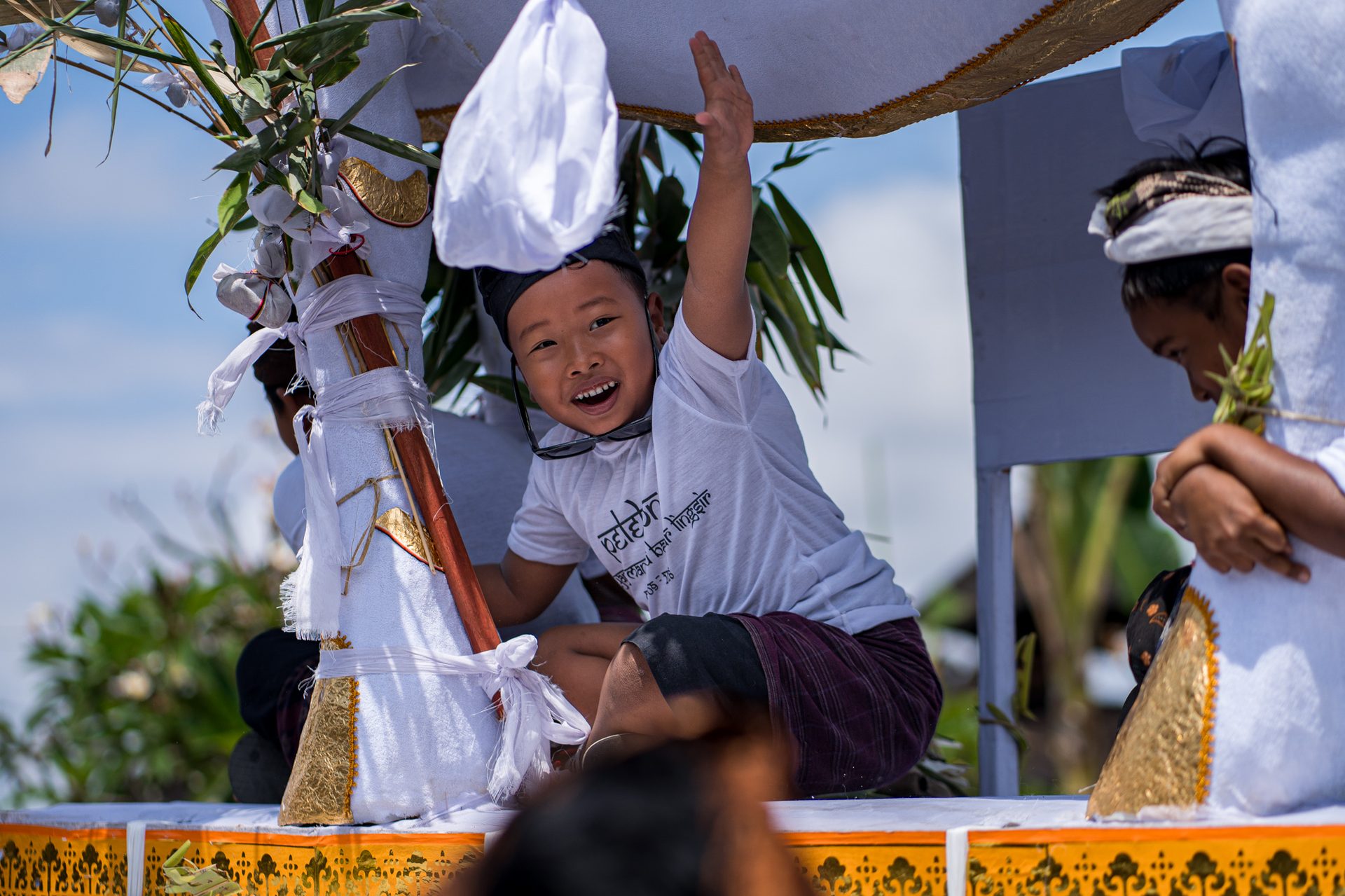 Jeune garçon souriant, bras levé, assis sur la structure du petulangan, Bali