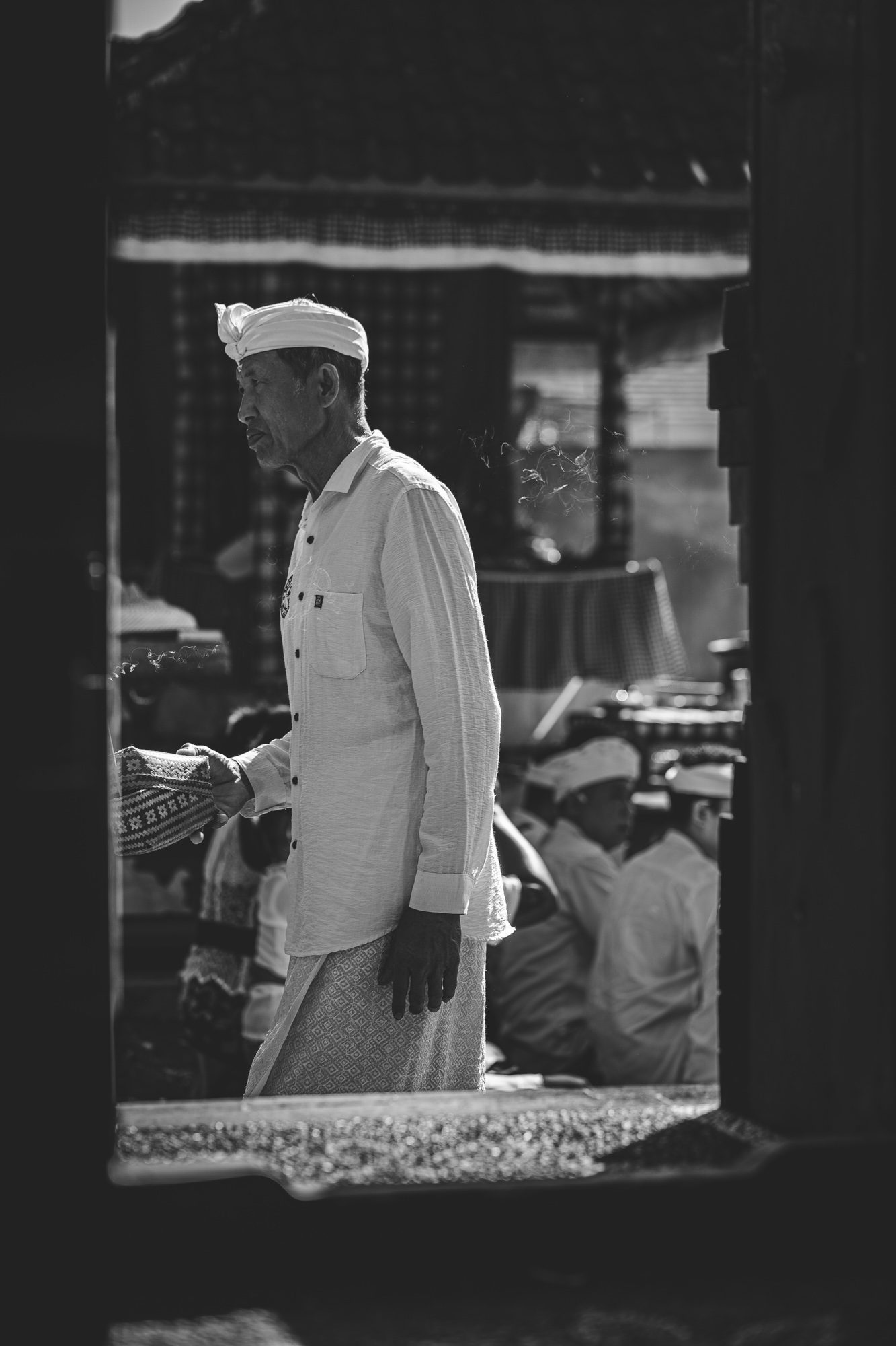 Homme en tenue blanche de cérémonie traversant une porte de temple, fumée d'encens, Bali (noir et blanc)